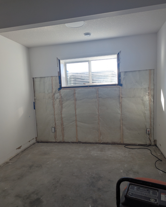 Basement under restoration after flood damage, with drywall removed and insulation exposed — showing early recovery steps. 